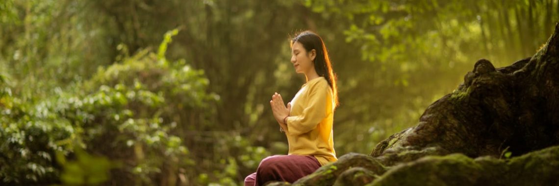 A woman meditates peacefully in a sunlit forest, embodying tranquility and connection with nature.