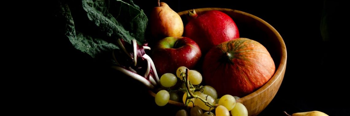 Dark still life composition featuring assorted autumn fruits in a wooden bowl, creating a moody and artistic scene.