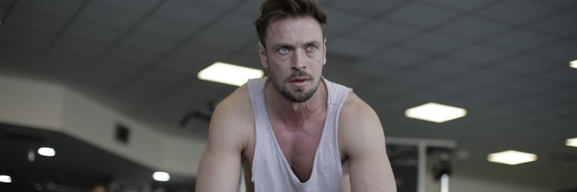 A man pauses to rest after a demanding exercise session at the gym, showcasing fitness and determination.